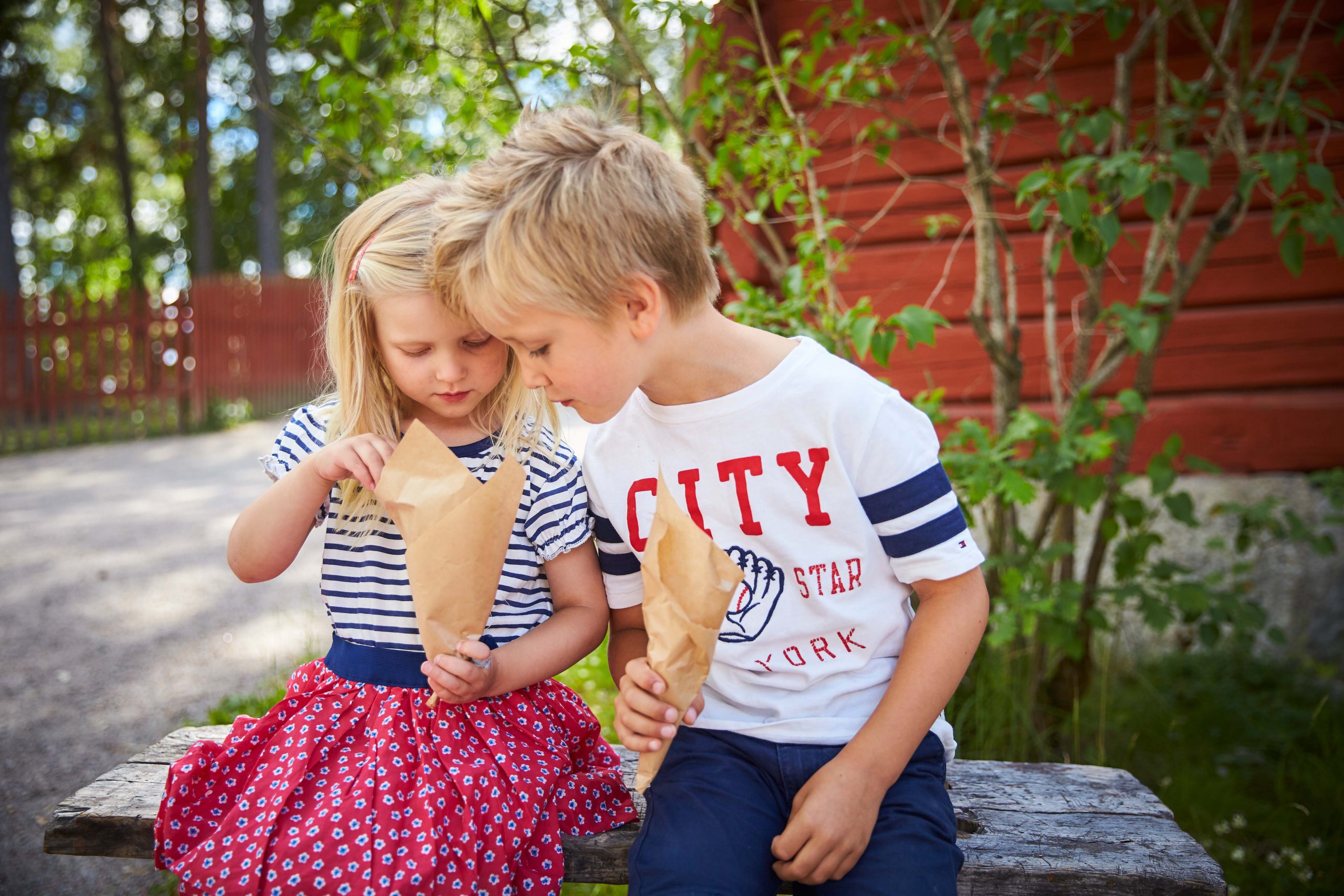 Barn sitter på en sten på Vallby Friluftsmuseum och äter godis från den gamla handelsboden. Foto: BildN