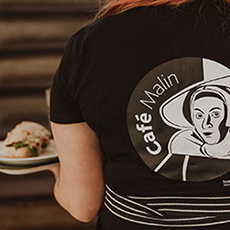 Ryggen på en i personalen som har en t-shirt med trycket Café Malin. Fotograf: Henrik Mill.