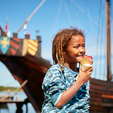 Pojke i blå tröja äter glass men ett vikingaskepp i bakgrunden på Kafe Gudagott. Fotograf: Pia Nordlander