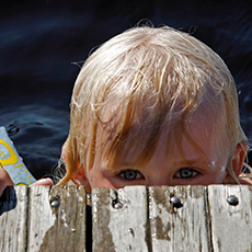 Ett barn som tittar upp i från bryggkanten på Lövuddens Badplats. Foto: Västmanlands kommuner och landsting