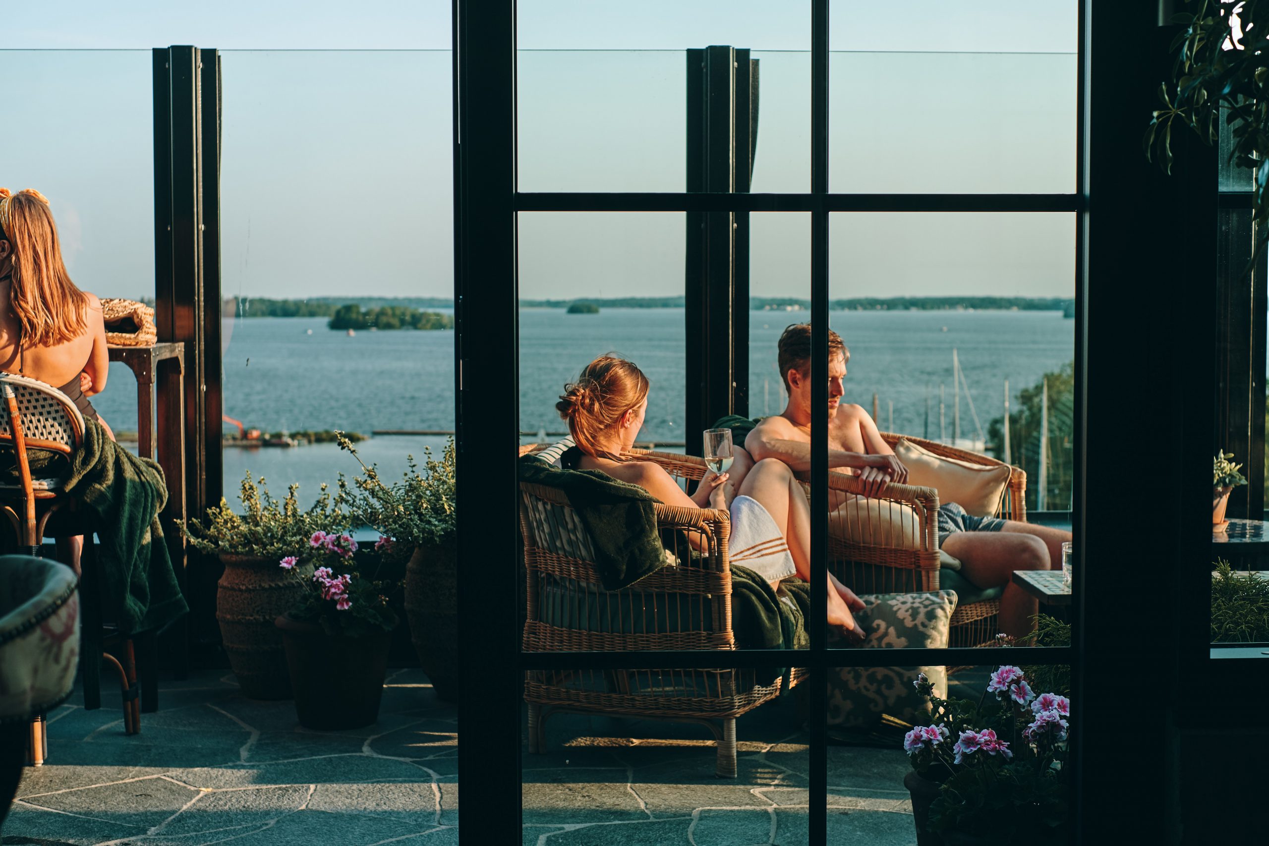 Några personer sitter i solen på utomhusterassen på Steam Hotel och deras Spa. Med vy över mälaren. Fotograf: Adam Af Ekenstam