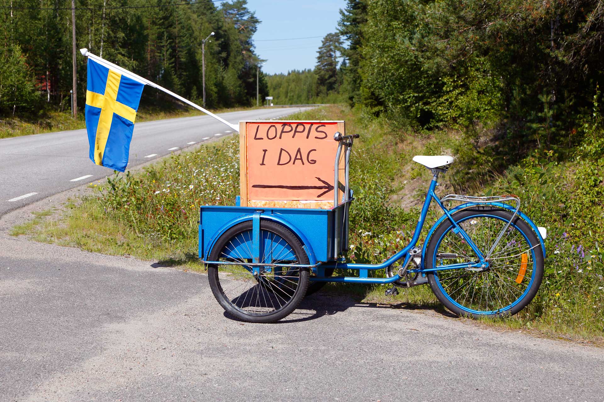 En blå flakcykel med flagga och skylt "Loppis idag". Fotograf: Mostphotos