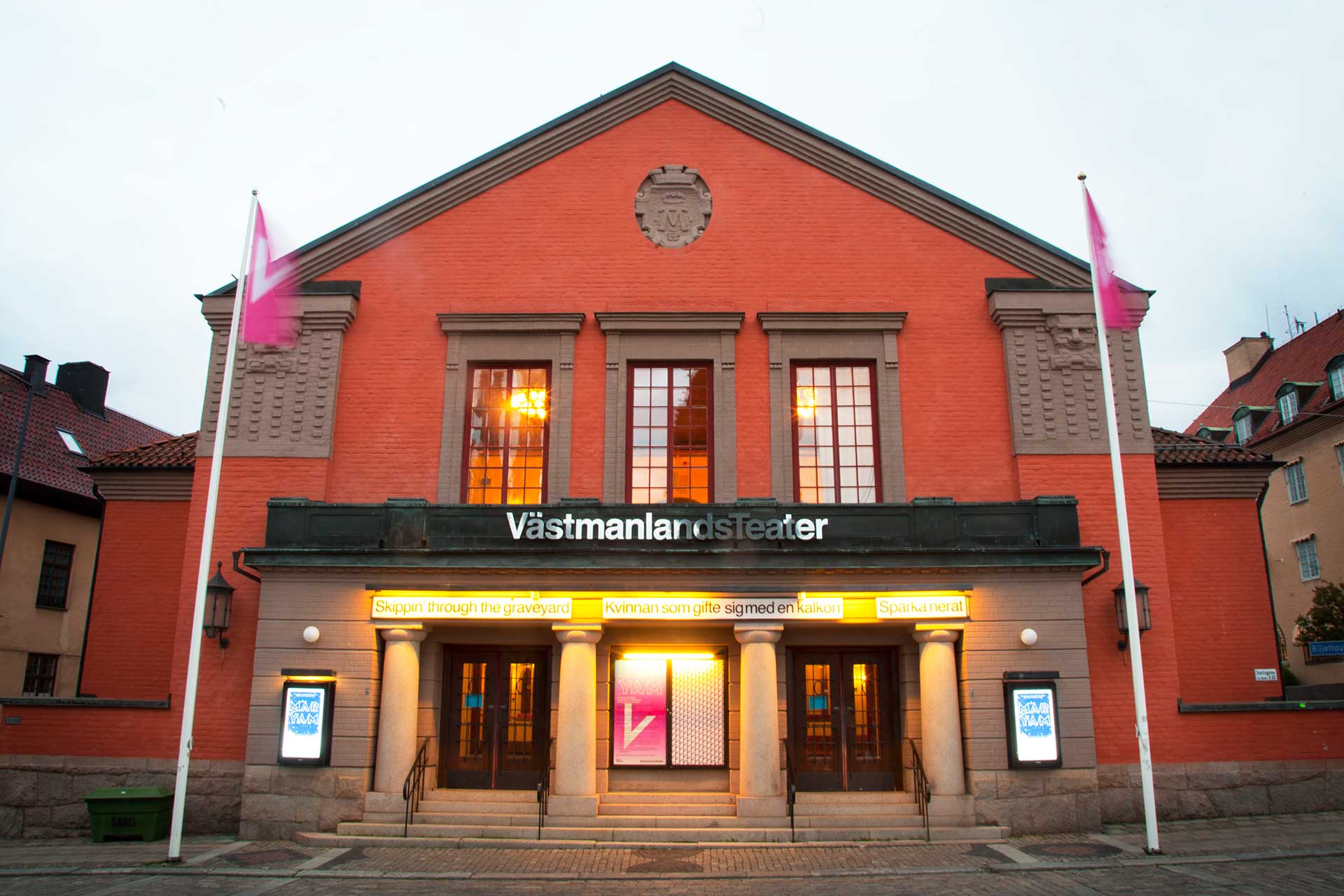 Västmanlands Teater i orange teagel med rosa flaggor som vajar. Fotograf: Kim Norman