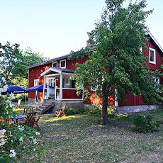 Stort rött hus i grönska på Aggarön. Foto: Pressbild
