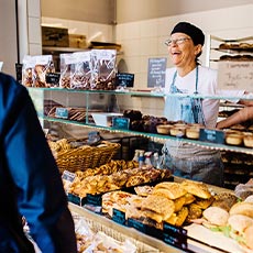 En glad kvinna på Kopparlundens bagerie betjänar en kund. Foto: Pressbild