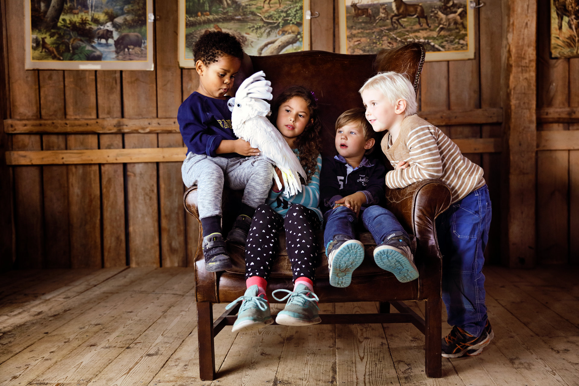Fyra barn sitter tillsammans i en stol med en papegoja på Kungsbyn. Foto: Pressbild